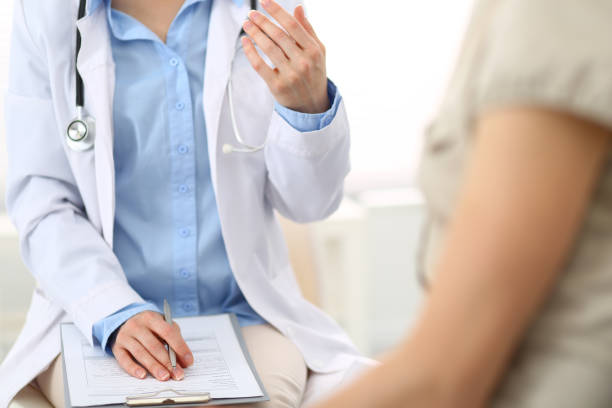 istock Doctor and patient talking. Physician at work in hospital while writing up medication history records form on clipboard near sitting woman. Healthcare and medicine concepts 1153898430