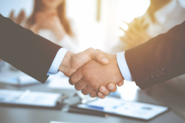istock Business people shaking hands at meeting while theirs colleagues clapping and applauding. Group of unknown businessmen and women in modern white office. Success teamwork, partnership and handshake concept 1153899263