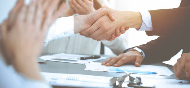 istock Business people shaking hands at meeting while theirs colleagues clapping and applauding. Group of unknown businessmen and women in modern white office. Success teamwork, partnership and handshake concept 1153899310