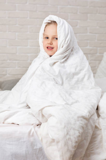 istock Child girl in blanket sitting on bed 1153919227