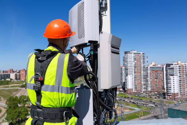 istock Telecommunication engineer  in helmet and uniform installs telecomunication equipment in his hand and  antennas of GSM  DCS UMTS LTE bands, outdoor radio units, optic fibers, power cables are installed on the roof. Working process of upgrading telecommuni 1153920773