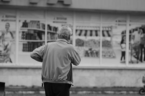 Elderly gray-haired man looks at shop window. Aged man does not have enough money. Old man stands near signboard of grocery store. Food prices rising. Russia, Barnaul, 31 July, 2014.