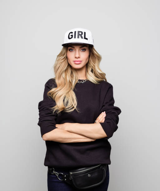 Portrait of urban woman standing arms crossed Portrait of urban woman standing arms crossed. Young female is with beautiful blond hair. She is wearing cap against white background. woman wearing baseball cap stock pictures, royalty-free photos & images