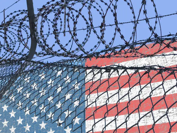 Photo of Ragged American flag surrounded by barbed wire steel illustrating the immigrations from Mexico issues. Concept image.