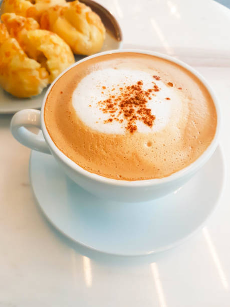 Hot cappuccino coffee served on table with ham cheese buns in cafe; shoot by mobile camera.