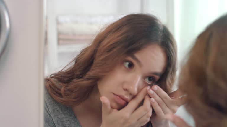 Young woman putting contact lens for eye front bathroom mirror in home