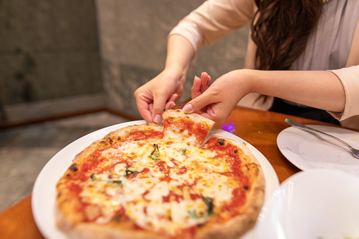 Close up of woman's hand picking up pizza in restaurant