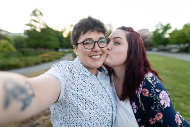 deux femmes embrassant et prenant un selfie sur une promenade de soirée - lesbian homosexual kissing homosexual couple photos et images de collection