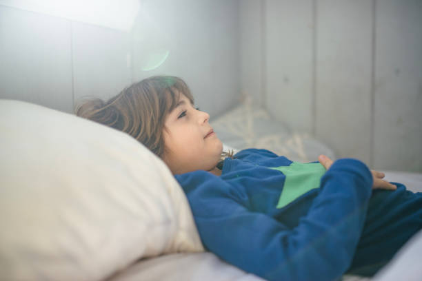 Kid in pajamas lays in bed feeling sick, stomachs Cute little 5 year old girl wearing pajamas lays in bed with her hand on her stomach, she is feeling sick and her expression is that she is unwell. Childhood illness and home sick gastroenteritis stock pictures, royalty-free photos & images