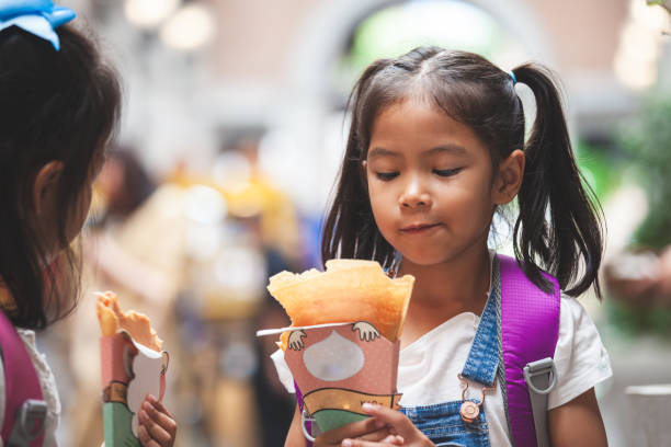 dos lindas niñas asiáticas con mochila comiendo panqueques juntos después de la escuela - eating child cracker asia fotografías e imágenes de stock