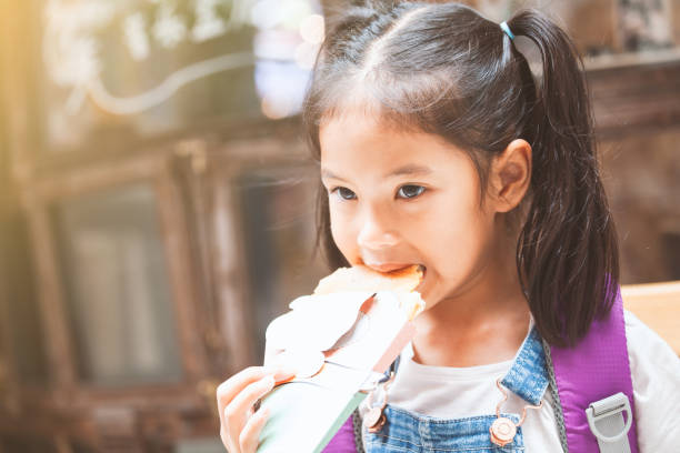 chicas asiáticas lindas con mochila comiendo panqueque después de la escuela en la escuela - eating child cracker asia fotografías e imágenes de stock