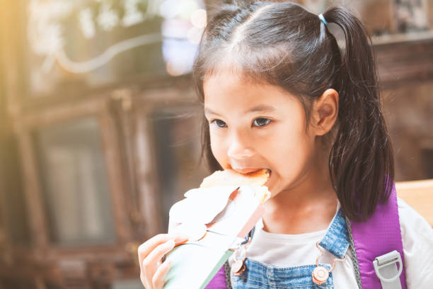 cute asian child girls with backpack eating pancake after school in the school - eating child cracker asia imagens e fotografias de stock