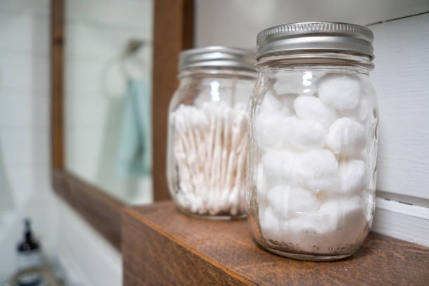 Cotton balls and cotton swabs in mason jars on farmhouse bathroom shelf. stock photo
