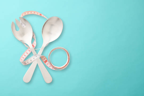 Overhead shot of cross shape silver salad server with tape measure on light blue background.