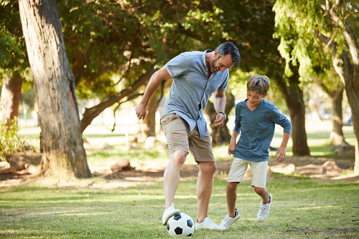 Shot of an adorable little boy playing soccer with his father in the park