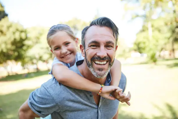 Shot of an adorable little girl enjoying a piggyback ride with her father in the park