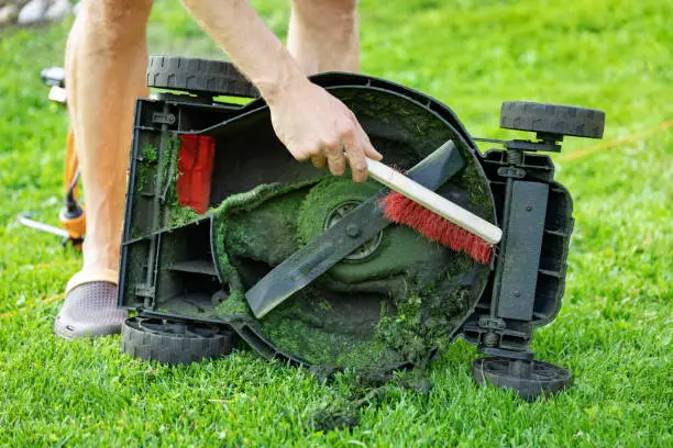 Photo of man with brush cleaning lawnmower from old grass