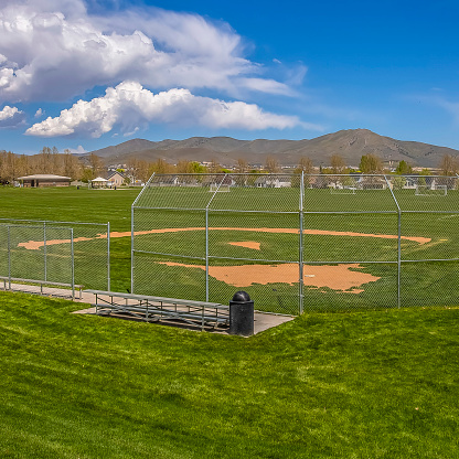 Frame Square Softball or Baseball field with view of mountain and sky on a sunny day. Bleachers for players and spectators are installed behind the fence.