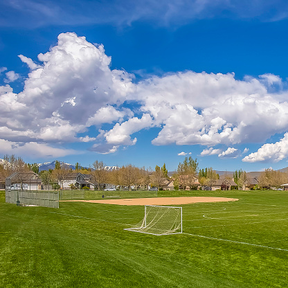 Square Soccer field and baseball field with view of mountain and cloudy blue sky. Houses and trees can also be seen around the perimeter of the sports field.