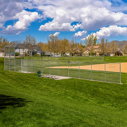 Frame Square Baseball field with view of mountain and cloudy blue sky on a sunny day. Buildings and lush trees can also be seen around the perimeter of the grassy field.