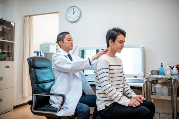 Male Japanese Doctor Examining a Patient Mature Japanese doctor delicately examining the neck and spinal alignment of a concerned male patient. medical examination room stock pictures, royalty-free photos & images