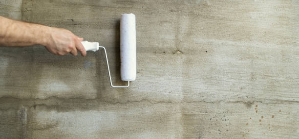 istock Background, gray plaster. Paint brushes, a man holds in his hand a paint roller against the background of a plastered wall. Panoramic photo and copy space 1154027080