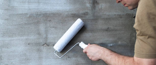 istock Background, gray plaster. Paint brushes, a man holds in his hand a paint roller against the background of a plastered wall. Panoramic photo and copy space 1154027236