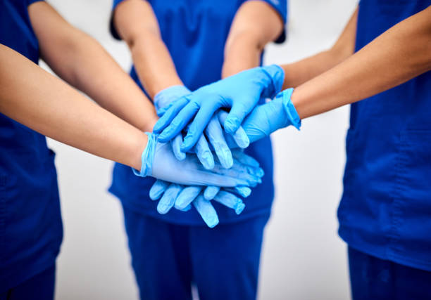 Your'e in safe hands with us Shot of an unrecognizable group of nursed joining their hands together in a hurdle against a grey background surgical glove stock pictures, royalty-free photos & images