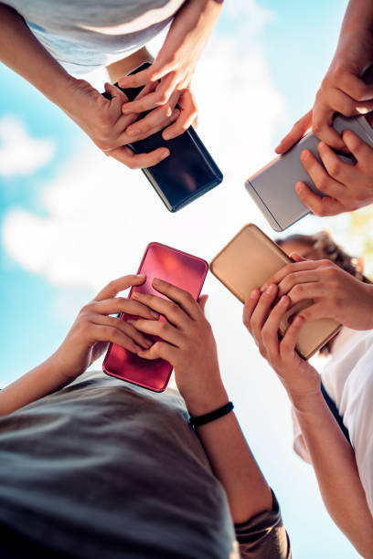 Kids using smart phones Group of kids standing in the schoolyard and using smart phones on a sunny day teenager back to school group of people student stock pictures, royalty-free photos & images