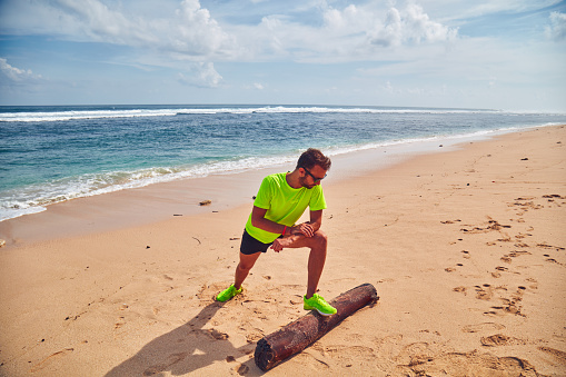 Sportsman stretching on a tropical sandy beach.