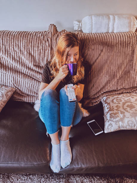 istock Woman watching TV and drinking coffee / tea on a couch. 1154035766