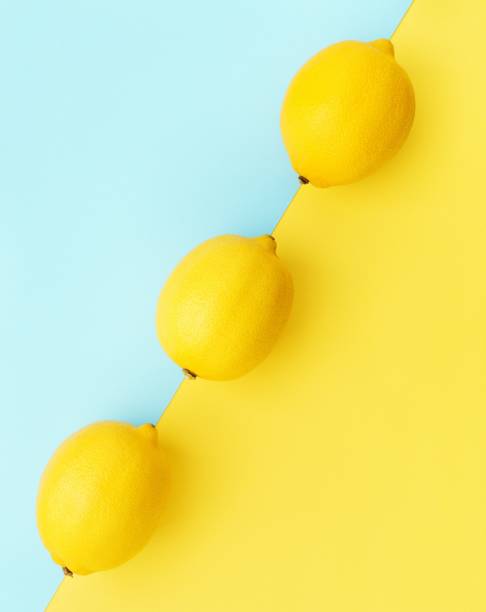 Lemons in row on pastel yellow and blue background Minimal summer concept Vertical.