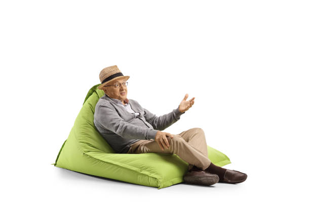 istock Senior man with face expression resting on a bean-bag armchair and gesturing with hand 1154038522
