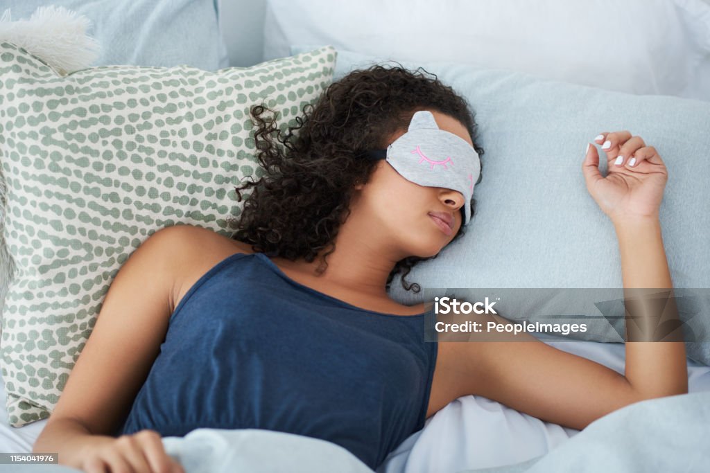 I sleep better with my eye mask on Shot of an attractive young woman sleeping in bed with an eye mask during the morning Sleeping Stock Photo