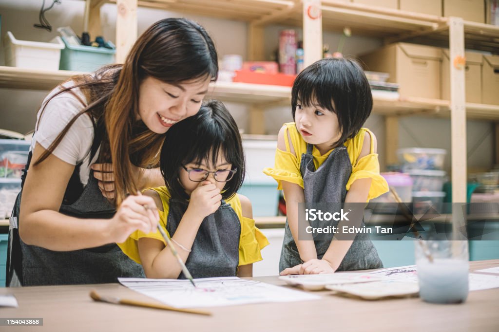 Die asiatische chinesische Kunstklehrerin unterrichtet ihre 2 Kunststudenten beim Zeichnen in ihrer Kunstklasse - Lizenzfrei Kind Stock-Foto