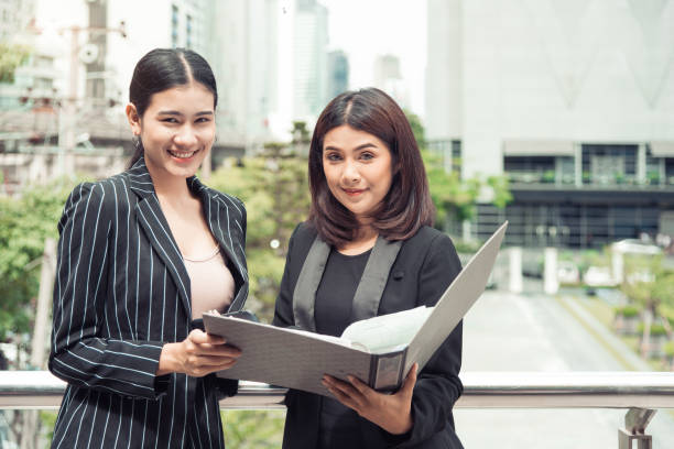 istock Two young Asian businesswomen looking into document file folder for analyzing profit or sale break even point after marketing. Business teamwork employees of lifestyle working women concept. 1154048237