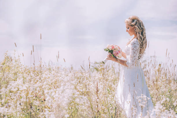 花嫁は白い花の分野で繊細な結婚式のブーケを保持しています。 - floral dress ストックフォトと画像