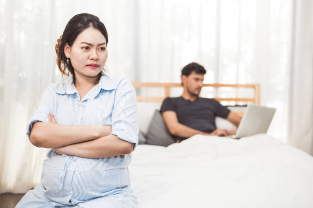 pregnant woman worried about husband neglect to take care of her health and baby. wife with ignored workaholic husband using laptop computer background. social issue problems of family in home bedroom - failure relationship difficulties computer women imagens e fotografias de stock