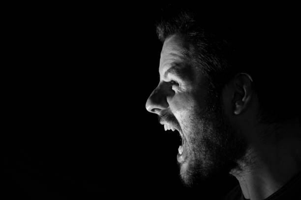 istock Angry man shouting out loud isolated on black background. 1154056436