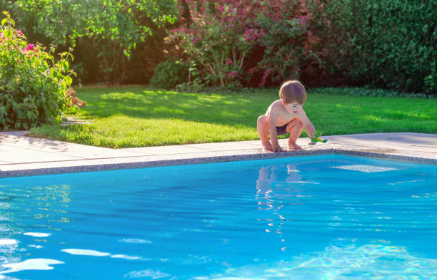 kleiner fröhlicher junge sitzt am pool im garten und spielt mit seinem spielzeug, das spaß hat. sommer. sommerferien. - swimming trunks fotos stock-fotos und bilder