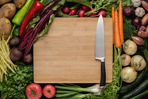 Kitchen Chef Knife with Fresh Vegetables on Wood Cutting Board. Vegetarian Raw Food. Healthy Eating Concept.