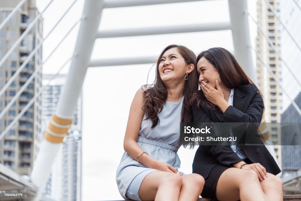Two Asian businesswomen gossip joke story at outdoors city after finished working. Business women coworker and friendship concept. Beautiful business people talking secret scandal topic in office life Gossip Stock Photo