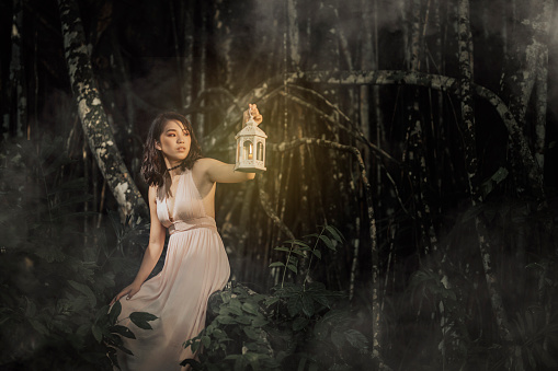 an asian chinese female at the jungle at night holding a lamp looking away
