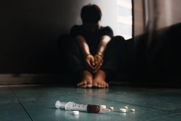 seringue et médicaments avec l’homme hors foyer assis sur le sol et les mains verrouillées dans les menottes. toxicomanes. journée internationale contre l’abus des drogues et le trafic illicite - prison narcotic addictions arrest photos et images de collection