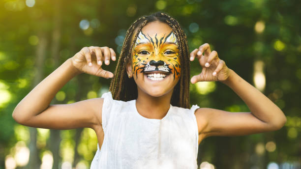 Cheerful little african-american girl with face painting like tiger Scary tiger cub. Cheerful little african-american girl with face painting like tiger roaring and showing claws on camera, laughing and playing in park african animals stock pictures, royalty-free photos & images