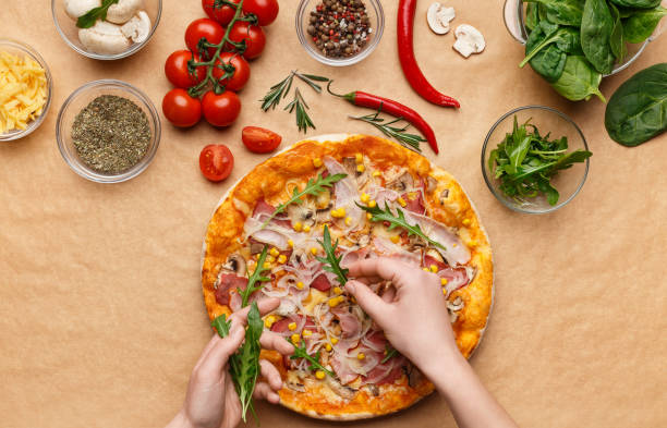 istock Woman adding rocket salad to pizza, top view 1154068615