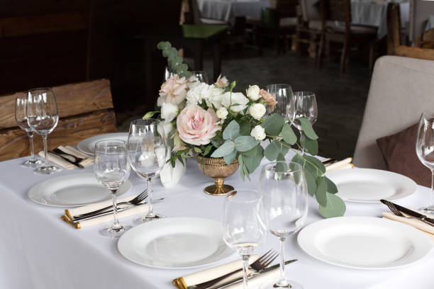 istock Wedding table setting decorated with fresh flowers in a brass vase. Wedding floristry. Banquet table for guests outdoors with a view of green nature. Bouquet with roses, eustoma and eucalyptus leaves. 1154074366