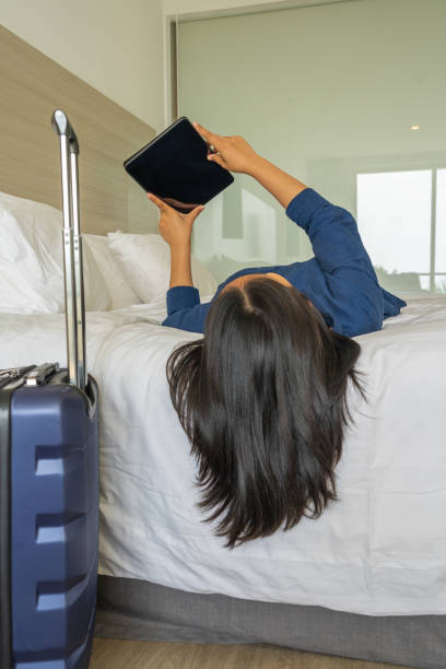 istock Woman lying on bed using tablet next to carry-on luggage 1154077437