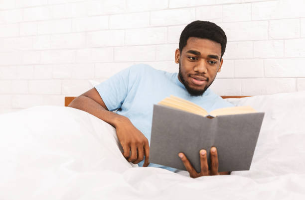 istock Young black guy reading book in bed 1154077688