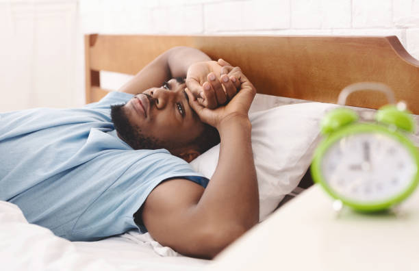 hombre negro en la cama que sufre de insomnio y trastorno del sueño - tired man fotografías e imágenes de stock